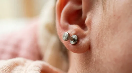 Detalle macro de cierre de rosca en pendiente infantil con mano de bebé borrosa al fondo